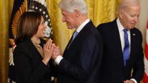 Bill clinton toma la mano de Kamala Harris. Biden aparece al fondo de la foto