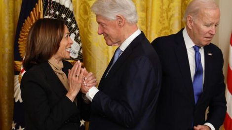 Bill clinton toma la mano de Kamala Harris. Biden aparece al fondo de la foto