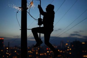 La silueta de un hombre, trepado en un poste eléctrico, y se produce un cortocircuito con chispas