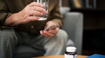 Hombre con un vaso de agua y analgésicos en la mano