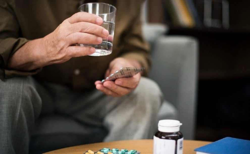 Hombre con un vaso de agua y analgésicos en la mano