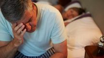 Hombre sentado en la cama con la mano en la cara