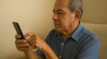 Un jubilado venezolano revisando su teléfono inteligente, sin mostrar la pantalla ni transmitir tristeza o alegría
